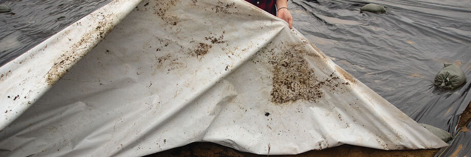 Person laying out a silage tarp on a planting bed.