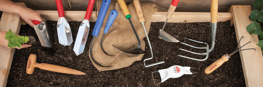 A collection of gardening hand tools laid out on a raised bed.