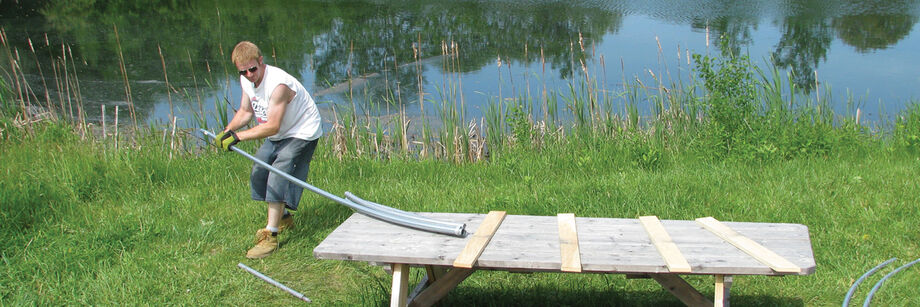 Man using a bender to form galvanized electrical conduit into the shape needed for a do-it-yourself high tunnel.