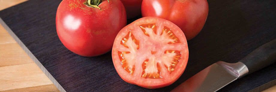 Three slicing tomatoes, shown on a cutting board. One is cut in half.