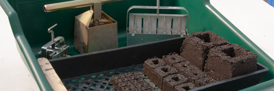 A soil blocking tray with three sizes of soil block makers and soil blocks.