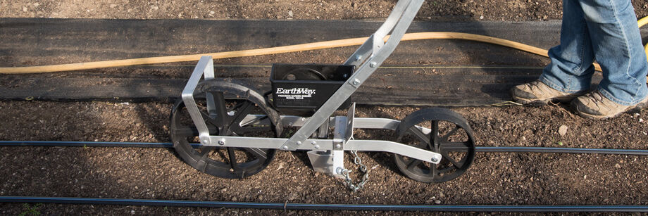 Person pushing an Earthway seeder along a row.