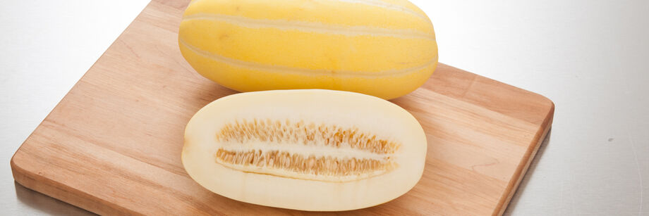 Two oblong yellow Asian melons shown on a wooden cutting board. One is whole and one is cut open to show the white flesh.