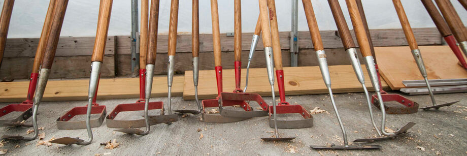 Several stirrup hoes and collinear hoes leaned up against a wall.