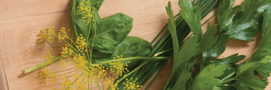 A few different herbs for salad mix, laid out on a wooden cutting board.