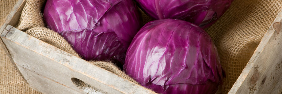 Three red cabbage heads in a wooden box.