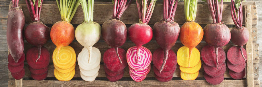 Beets from ten different beet varieties, laid out on a wooden crate, and each shown with cross-section slices so that you can see the internal colors.