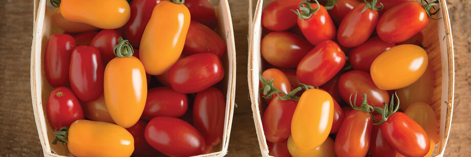 A colorful assortment of grape tomatoes, displayed in wooden quart containers.