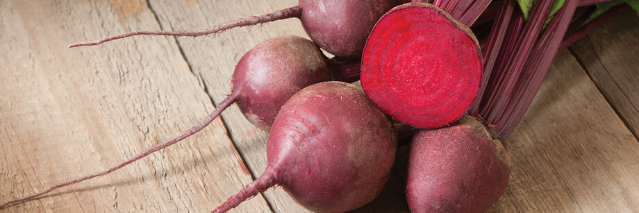 bunch of red round beets, with one beet sliced open to reveal bright red interior.