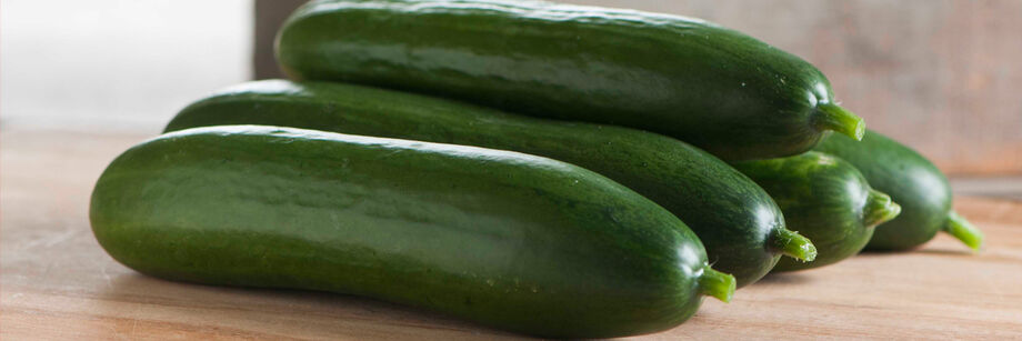 Five whole seedless cucumbers are laid out on a cutting board.