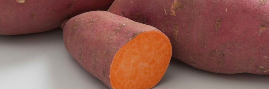 Three sweet potato tubers, one cut open to reveal the bright orange interior.