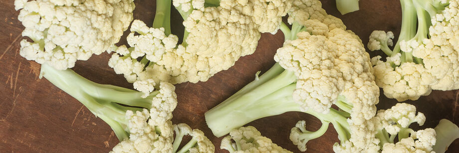 Close-up of one of our green stem cauliflower varieties. It has long stems and white florets and is shown sliced and laid on a table.