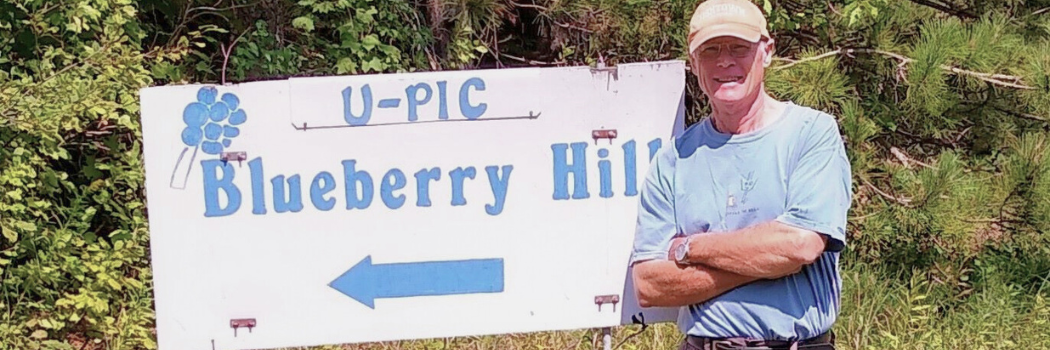 Larry Waldo of Harrietta's Blueberry Hill standing next to their blueberry u-pick sign.
